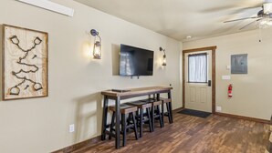 Una habitación con piso de madera, un televisor montado en la pared, una mesa con bancos y una puerta con ventanal.