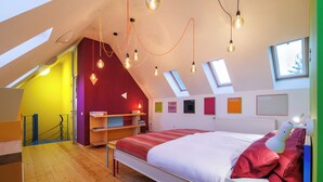 A bedroom with a sloped ceiling, skylights, a bed with a red blanket, and a bedside lamp. - Monument with designer furnishings  (Kranenburg)