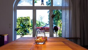 Ein Holztisch mit einem Glas, das eine Blumenanordnung enthält, einer hängenden Leuchte und einem Blick auf ein rotes Auto durch eine Glastür.