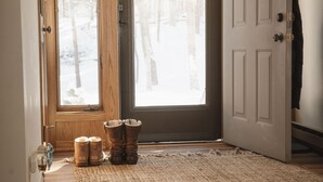 Eine Holztür mit Blick auf einen verschneiten Wald, ein Teppich und ein Paar Stiefel.