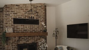 Ein Wohnzimmer mit Kamin aus Ziegelsteinen, einem an der Wand befestigten Flachbildfernseher und einem grauen Sofa.