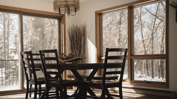 Ein Essbereich mit Tisch und Stühlen, große Fenster mit Blick auf einen verschneiten Wald und eine Hängelampe.