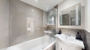 A modern bathroom with a glass-enclosed shower, a white bathtub, and two sinks with mirrors above them.