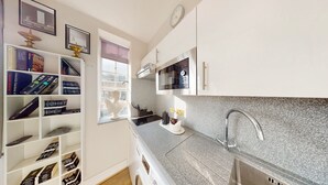 A modern kitchen with granite countertops, a stainless steel sink, and a built-in microwave. There is a window with a view of the city, and a bookshelf filled with books.