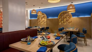 A restaurant interior with wooden tables, blue upholstered chairs, and woven pendant lighting.