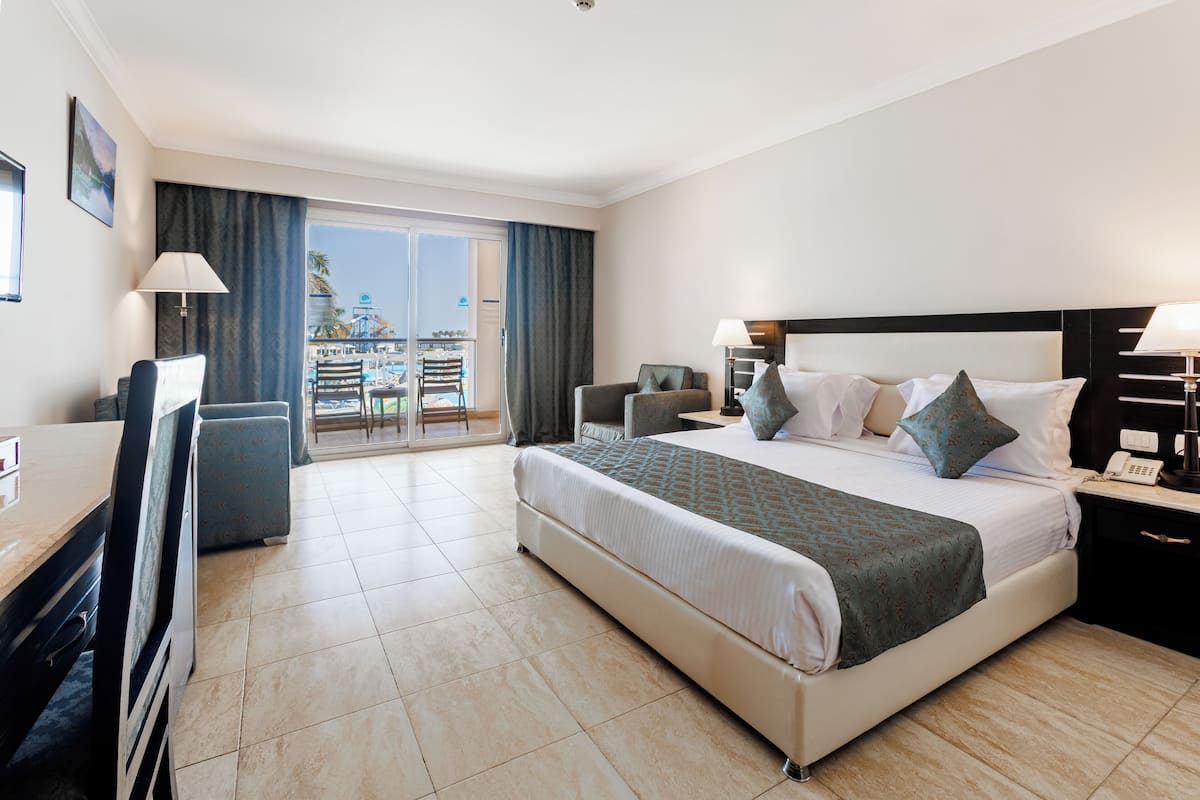 A hotel room with a large bed, a desk, and a balcony with a view of a resort.