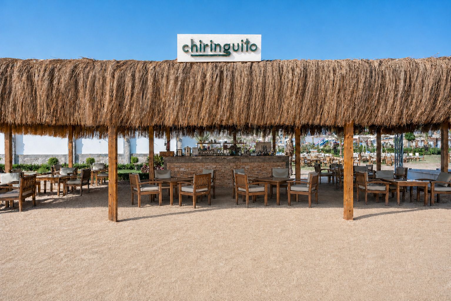 Un espacio de estar al aire libre con techo de paja, un letrero que dice 'chiringuito' y mesas y sillas de madera.