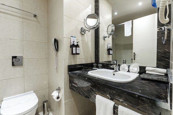 Une salle de bain avec des toilettes blanches, un lavabo doté d’un plan de travail en marbre noir et deux miroirs.