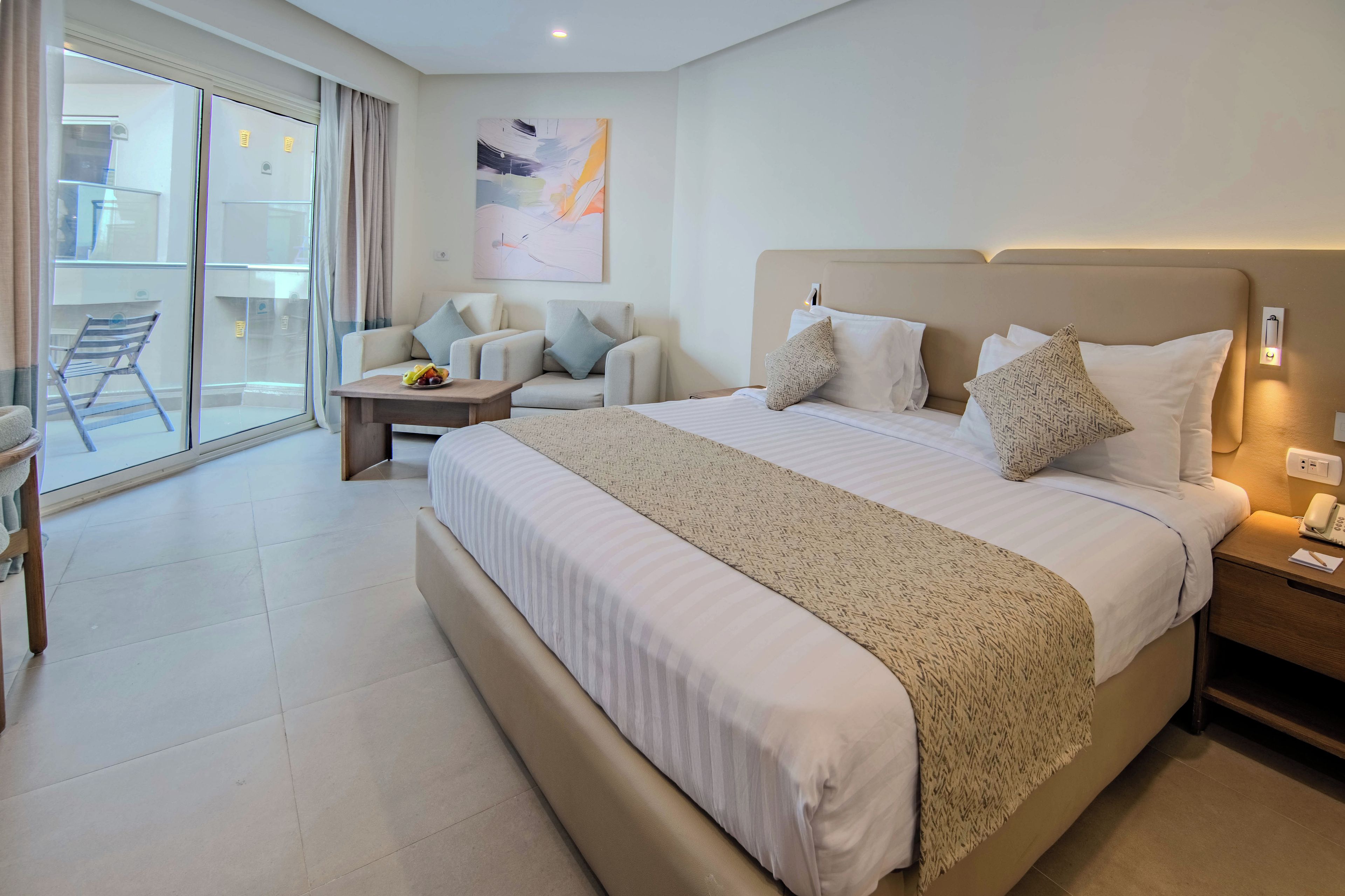 A hotel room with a large bed, a sofa, a small table, and a view of a balcony.