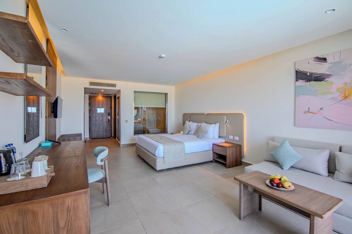 A modern hotel room with a bed, bedside table, and a desk with chairs.