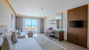 Una habitación de hotel moderna con una cama grande, un escritorio, una silla, un televisor y un balcón con vistas al mar.