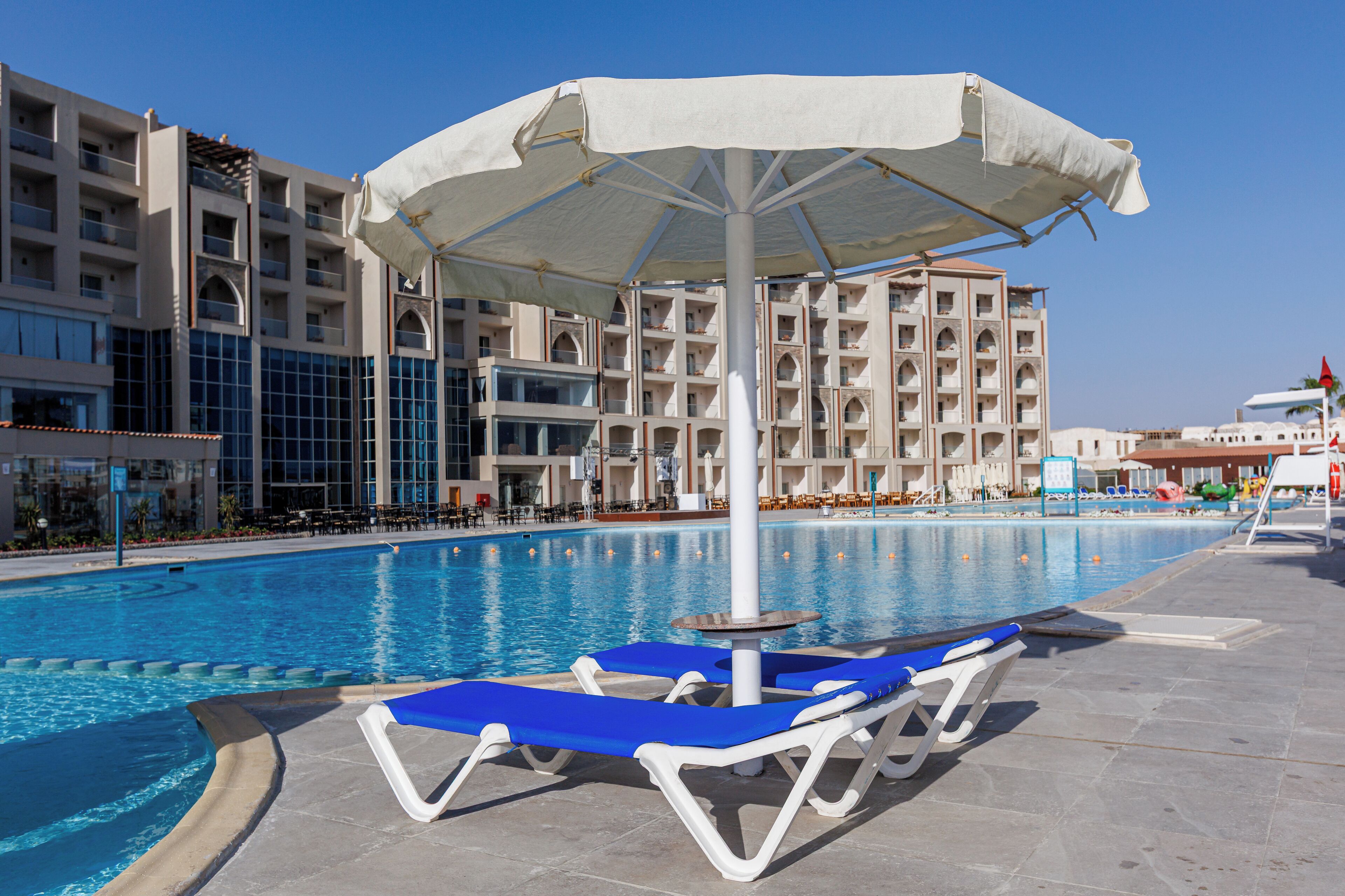 A swimming pool with blue lounge chairs and a white umbrella.