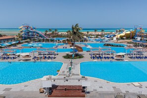 A large outdoor swimming pool area with multiple smaller pools, a water slide, and beach views.
