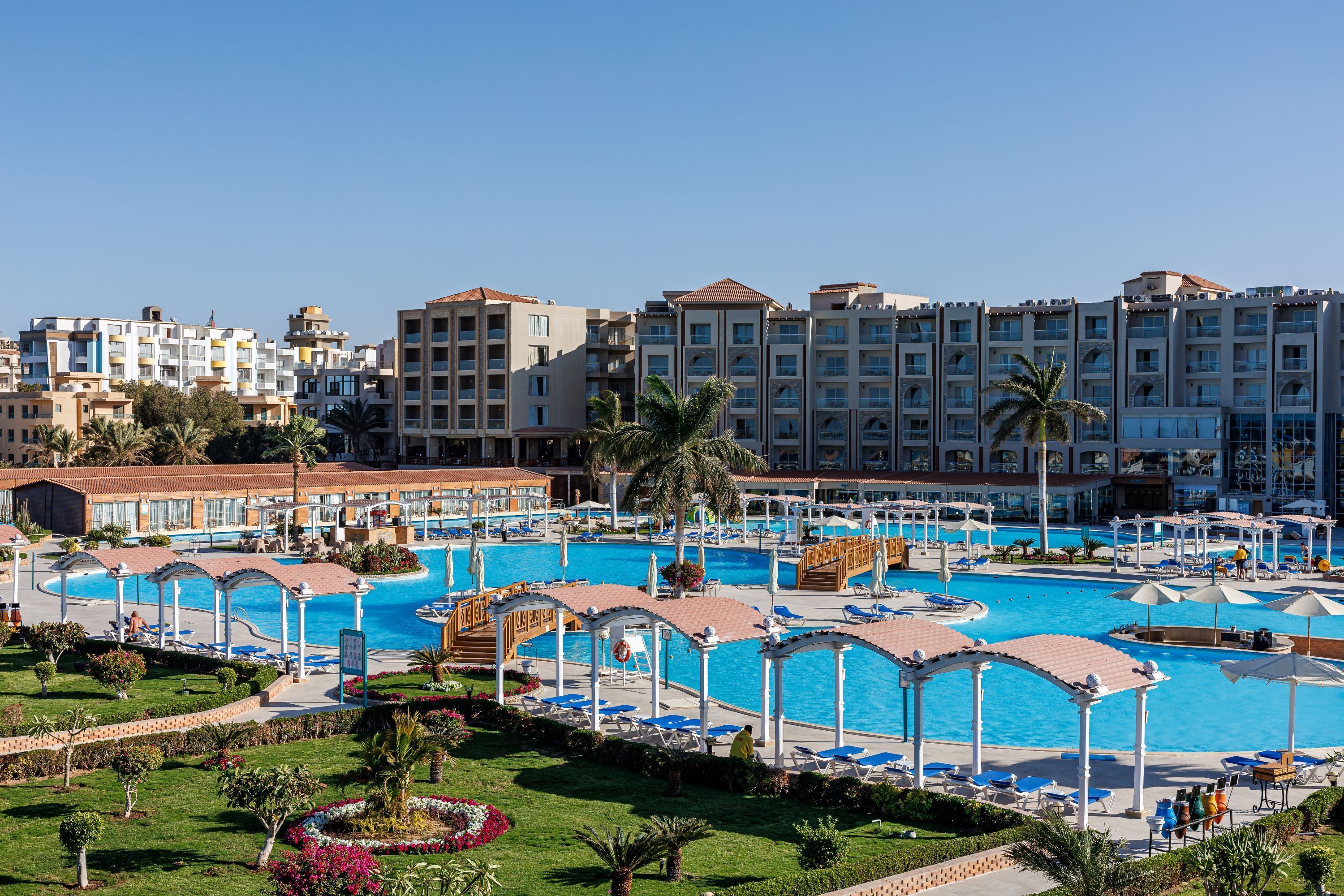 Ein Hotel mit mehreren Schwimmbecken, überdachten Gängen und einem gepflegten Garten.