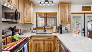 Una cocina con armarios de madera, un refrigerador de acero inoxidable, un lavamanos doble y una ventana con persianas.
