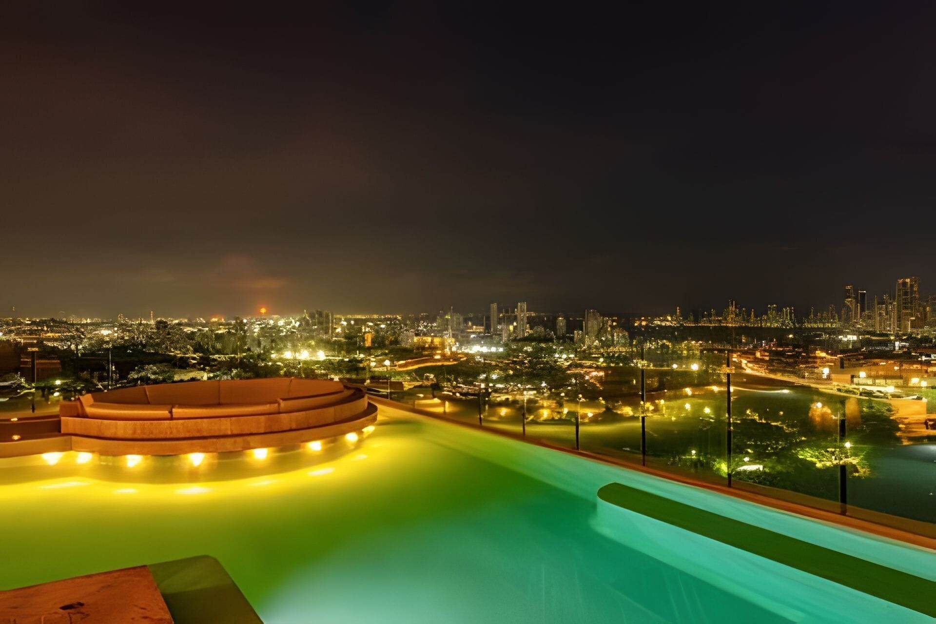 A nighttime view of a cityscape with a pool area featuring a circular seating area and a water feature.