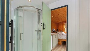 Ein modernes Badezimmer mit Duschkabine aus Glas, Holzvertäfelung und einem sichtbaren Bett im angrenzenden Raum.