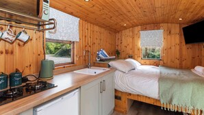 Ein gemütliches Blockhaus mit Küchenbereich, einem Bett mit karierter Decke und einem an der Wand befestigten Fernseher.