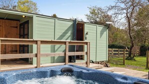 Ein Wellnessbereich mit Whirlpool, Holzterrasse und einem grünen Gebäude mit einer Tür.