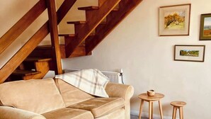 Una sala de estar acogedora con un sofá y sillones, una escalera de madera y dos pequeñas mesas de madera.