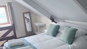 Una cama bien hecha con un edredón blanco y azul turquesa, dos almohadas azul turquesa y toallas blancas dobladas.