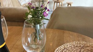 Un salón acogedor con una escalera de madera, un jarrón de cristal con flores sobre una mesa de madera y una cesta tejida.