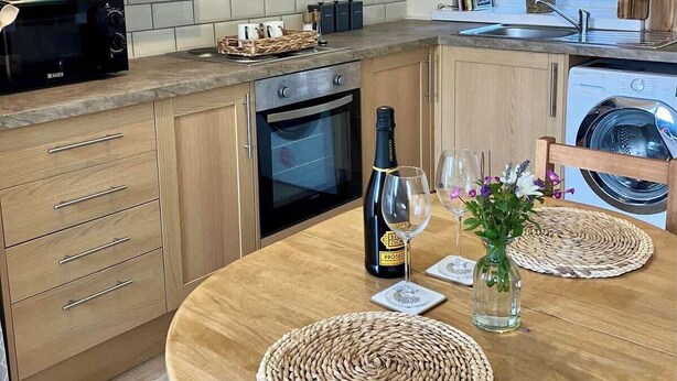 Una cocina moderna con armarios de madera, horno empotrado, microondas y lavadora.