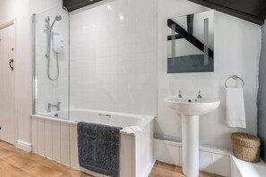 Ein modernes Badezimmer mit einer in Glas abgeschlossenen Dusche, einer weißen Badewanne, einem Standwaschbecken und einem Spiegel darüber.