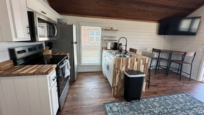 Una cocina compacta con encimeras de madera, horno integrado y microondas. Incluye una pequeña isla con fregadero y taburetes de bar.