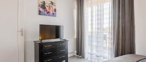Quarto com uma cama, uma televisão sobre uma cômoda e uma janela com cortinas.