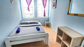 A bedroom with a bed, a chair, a wooden shelf, and a window with curtains.