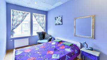 A bedroom with a large bed, a chair, a bedside table, and a window with curtains.