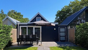 Un jardin à l’arrière de la maison, avec une terrasse, un espace salon abrité et un petit potager.
