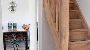 Un intérieur moderne avec un escalier en bois, un coin repas comprenant une table et des chaises, et un luminaire suspendu.