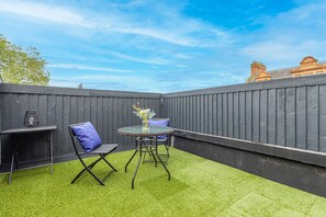 Eine Terrasse mit einem runden Tisch, zwei Stühlen und einem kleinen Tisch mit einer Lampe.