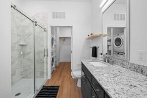 Une salle de bain moderne avec une douche en verre, un lave-linge encastré et un comptoir en granit.