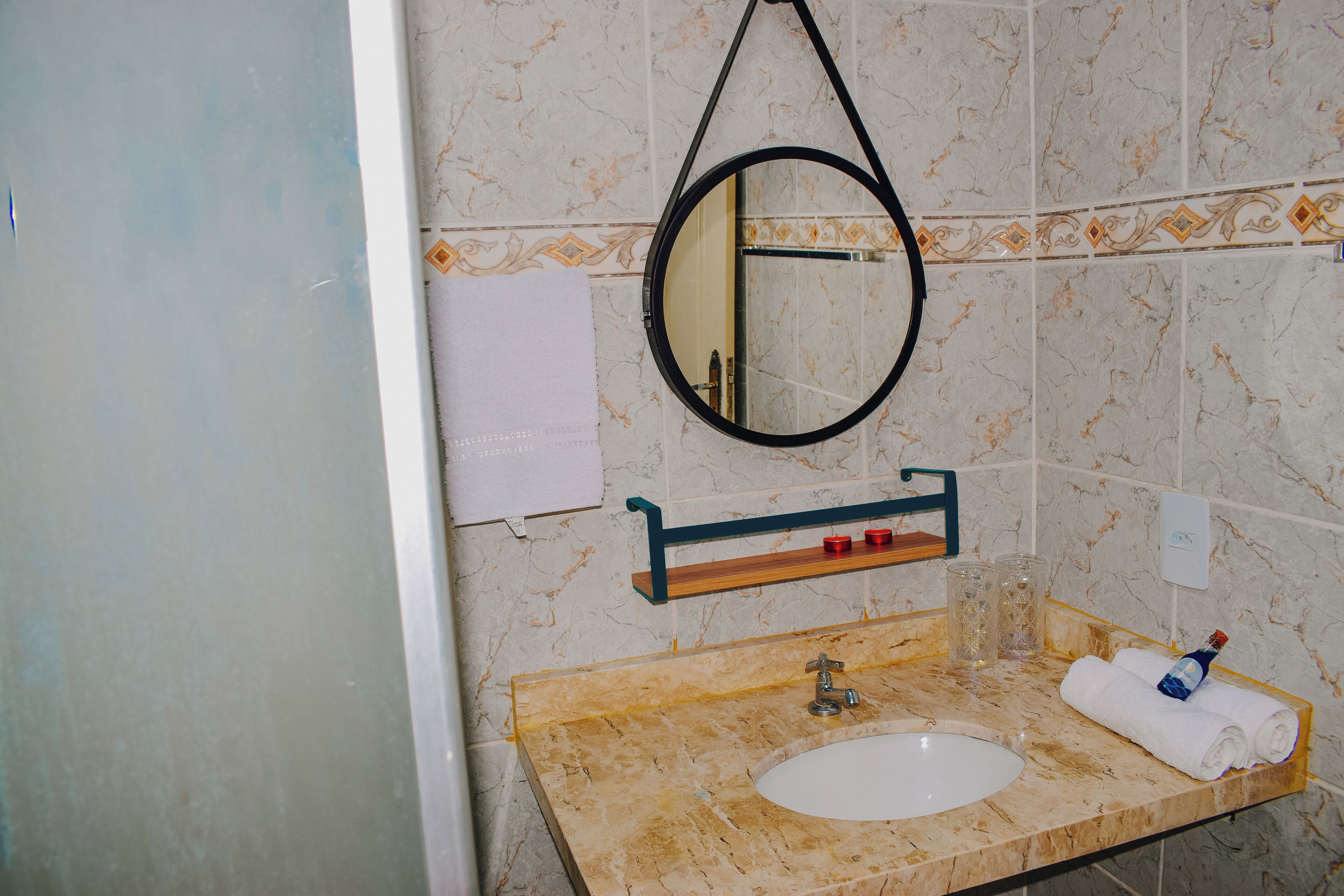 Casa de banho com lavatório de mármore, espelho, porta-toalhas e uma prateleira com produtos de higiene pessoal.
