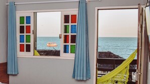 Una habitación con vistas al mar a través de una ventana con vidrios de colores y cortinas azules.