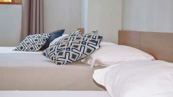 A bed with patterned and plain pillows, a wooden headboard, and a plain wall.