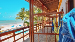 Una terraza de madera con vista a la playa y al océano, una piscina y hamacas colgantes.