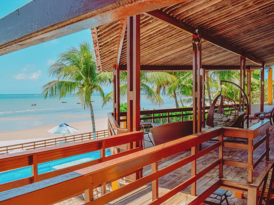 Un resort frente al mar con una terraza de madera, una piscina y vista al océano y palmeras.