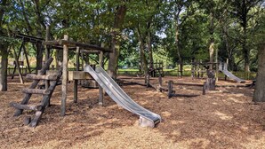 Un terrain de jeux doté de plusieurs toboggans et d’aires d’escalade, le tout entouré d’arbres.
