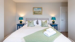 Un lit bien fait, recouvert d’un plaid à motifs verts, avec deux lampes assorties et un tableau accroché au mur.