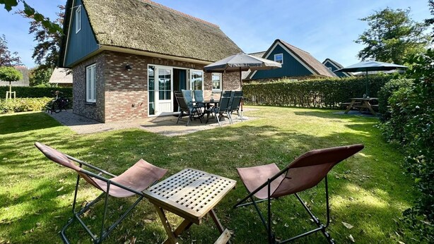 A house with a thatched roof, a patio with a table and chairs, and a well-maintained lawn.