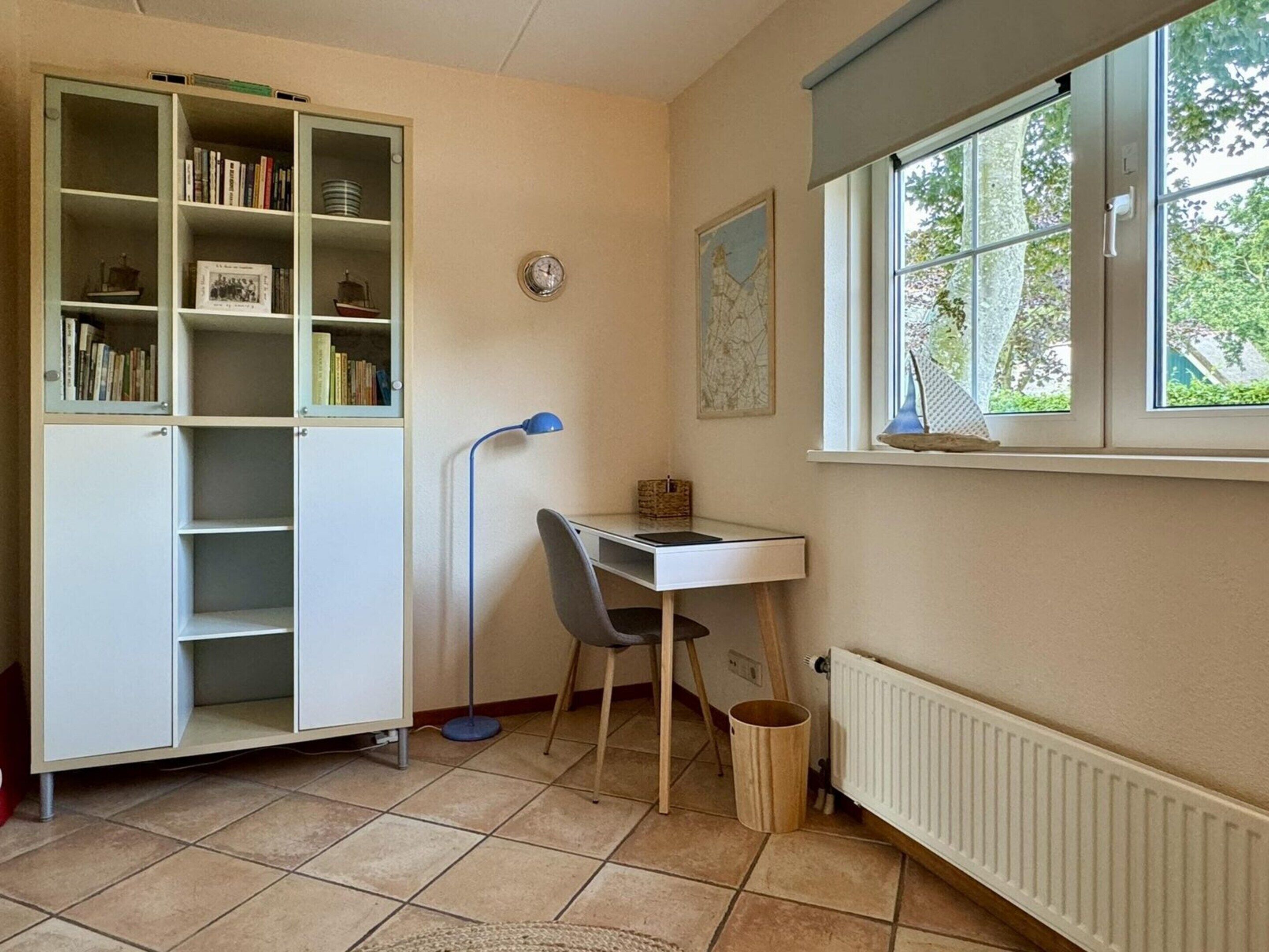 Una sala de estudio con un escritorio, una silla, una estantería y un ventanal con vistas a árboles.