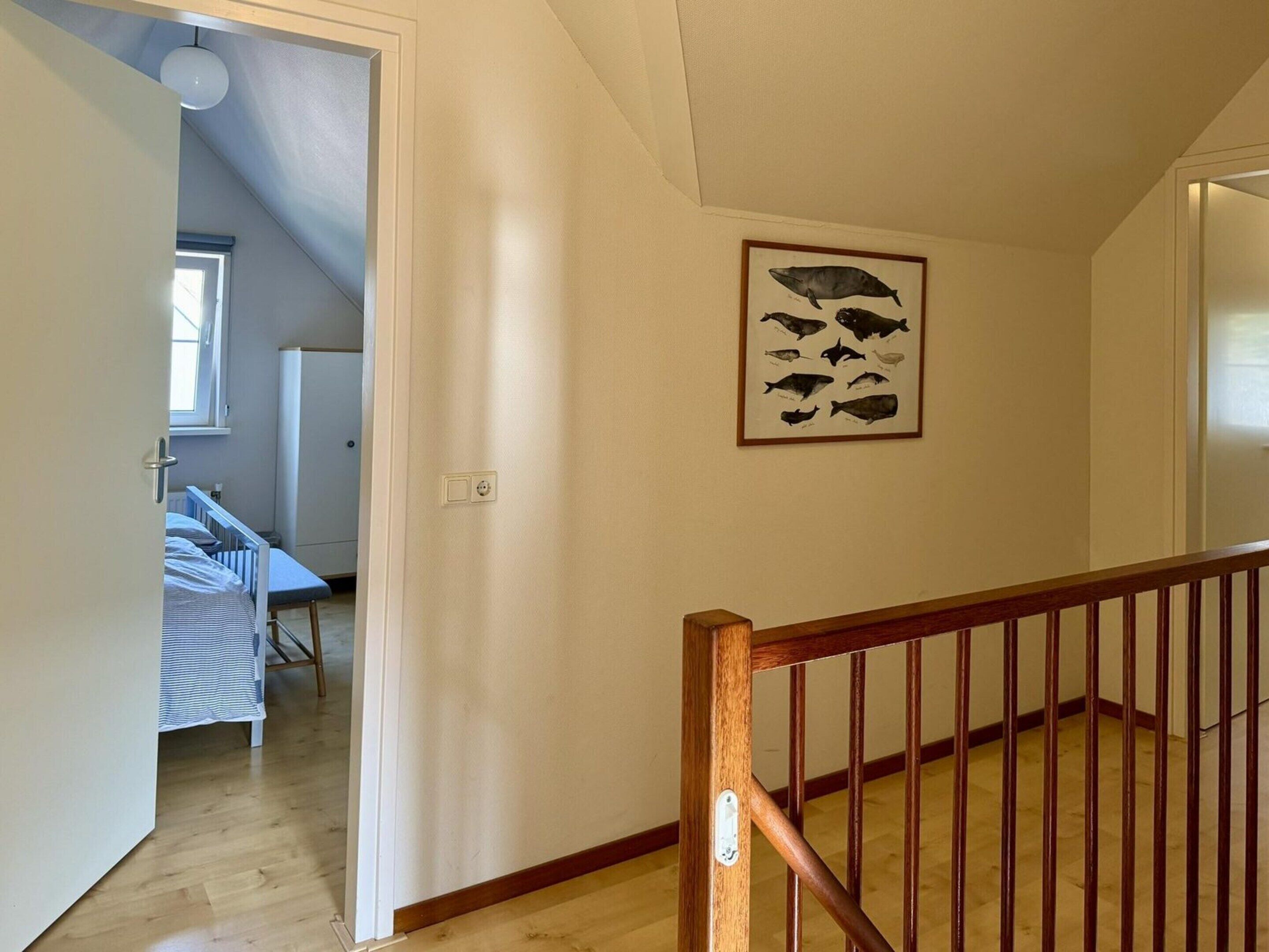 A hallway with a wooden staircase, a baby crib, and a wall-mounted fish illustration.