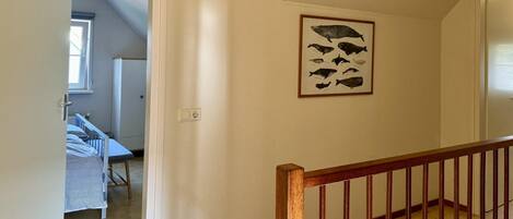 A hallway with a wooden staircase, a baby crib, and a wall-mounted fish illustration.