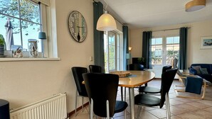A dining area with a round table, black chairs, a wall clock, and a window with curtains.