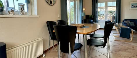 A dining area with a round table, black chairs, a wall clock, and a window with curtains.