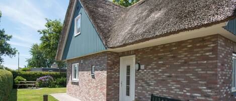 A brick house with a thatched roof, a front door, and a bench outside.